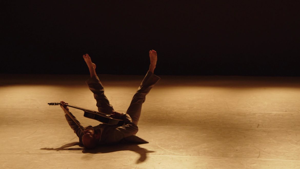 Dancer in suite with guitar lying on his back